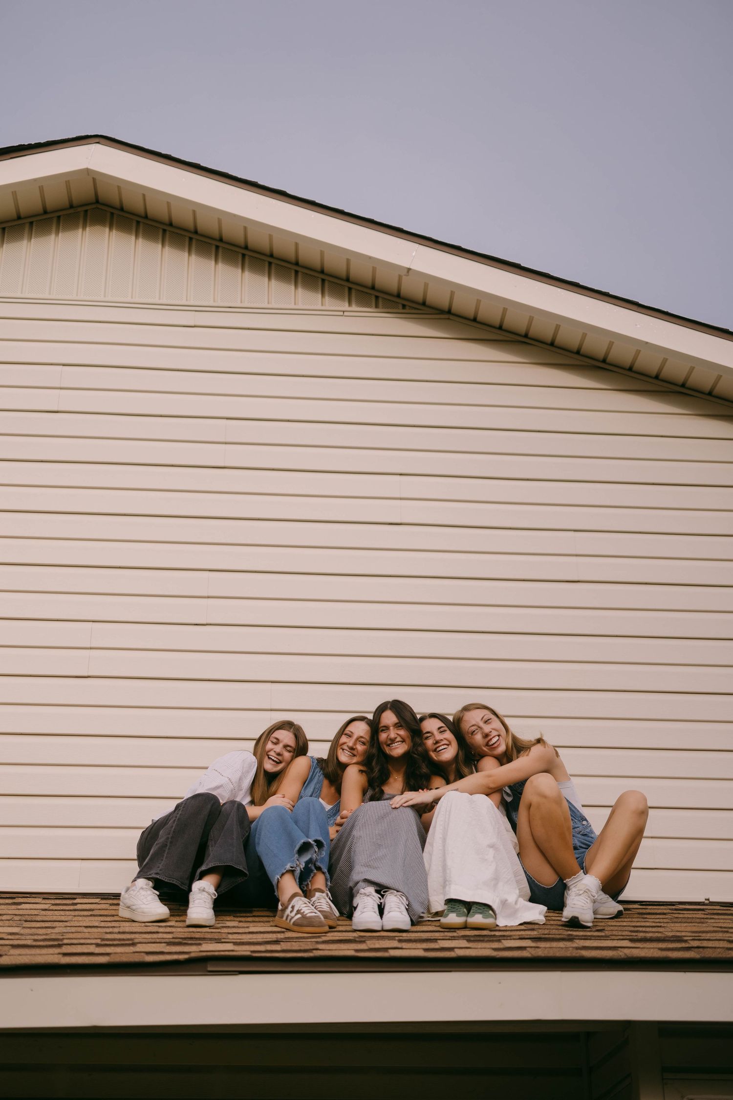 A group lying down in a row on a white house roof for a creative photo.