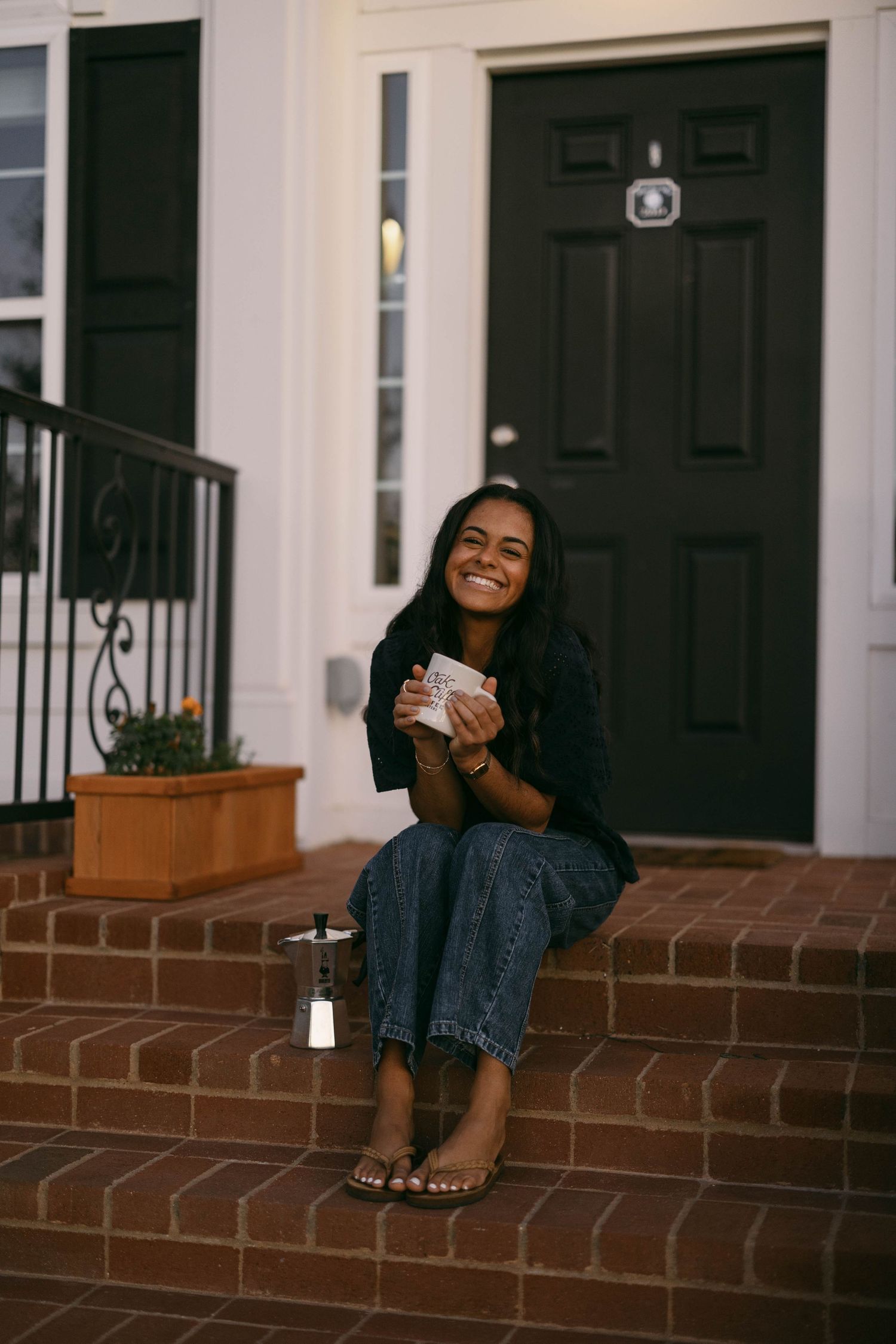 Person relaxing on brick steps of house entrance with coffee mug.