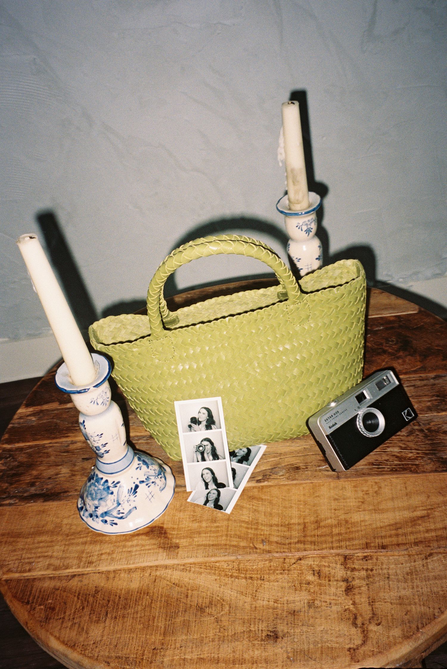 Vintage decor arrangement featuring a green basket, blue ceramic vase, and photographs on wooden surface.
