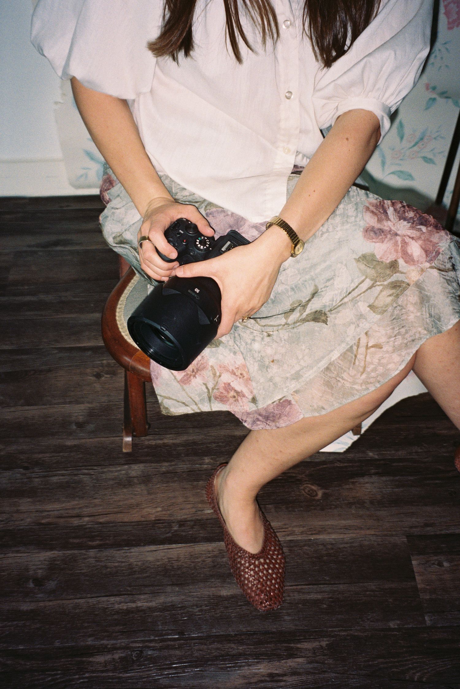 Detailed view of hands holding a camera while seated on dark wooden flooring.