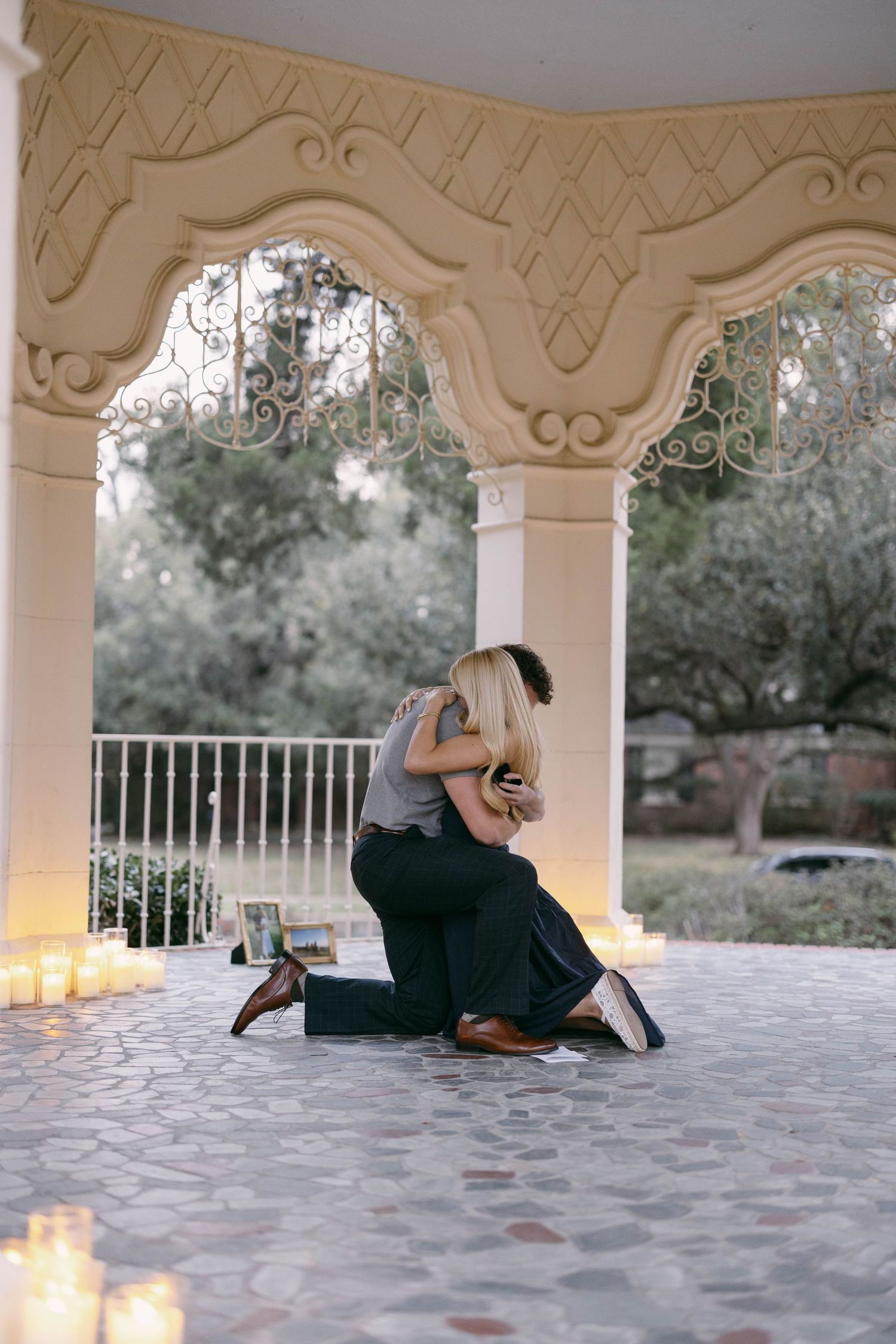Couple sharing an emotional embrace during a romantic marriage proposal under an elegant gazebo surrounded by candles.