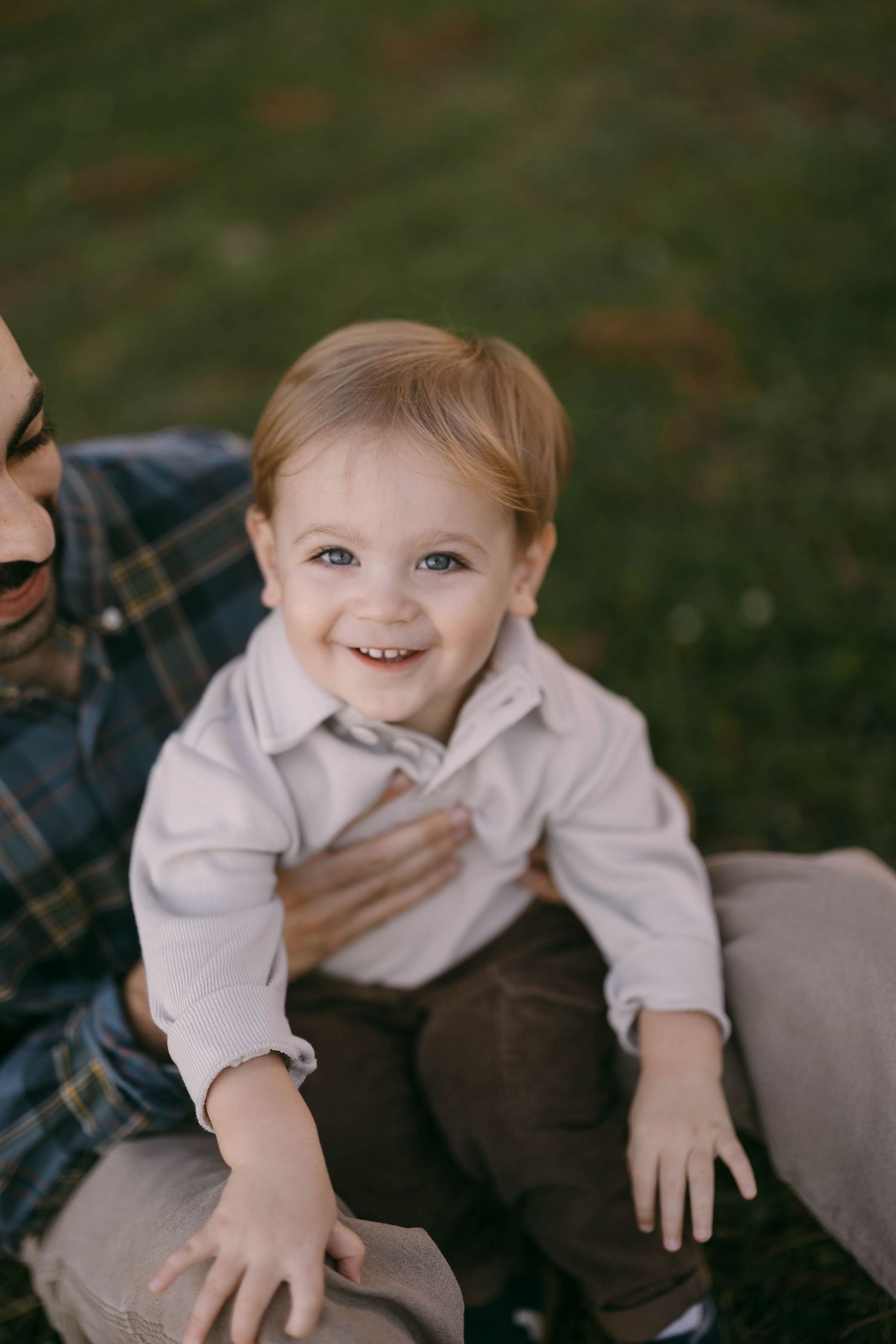 A child laughing and playing while being held by someone in casual clothes outdoors.