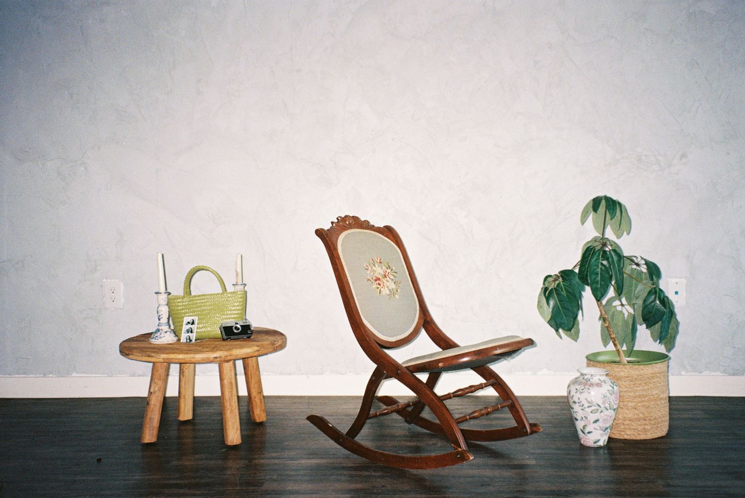 A vintage rocking chair and side table arranged with plants against a white textured wall.