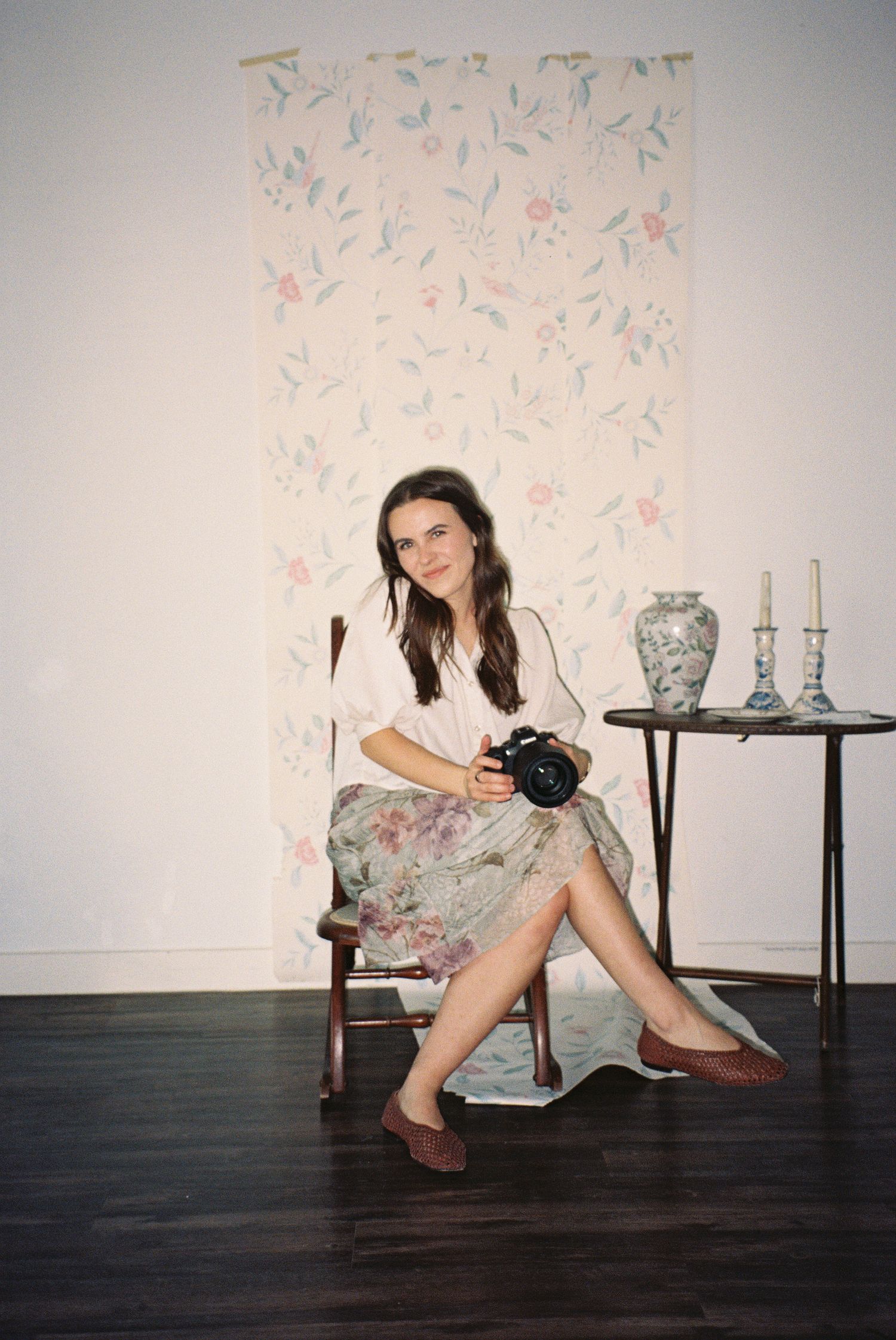 Lifestyle photo shoot against floral wallpaper and dark wooden floor.