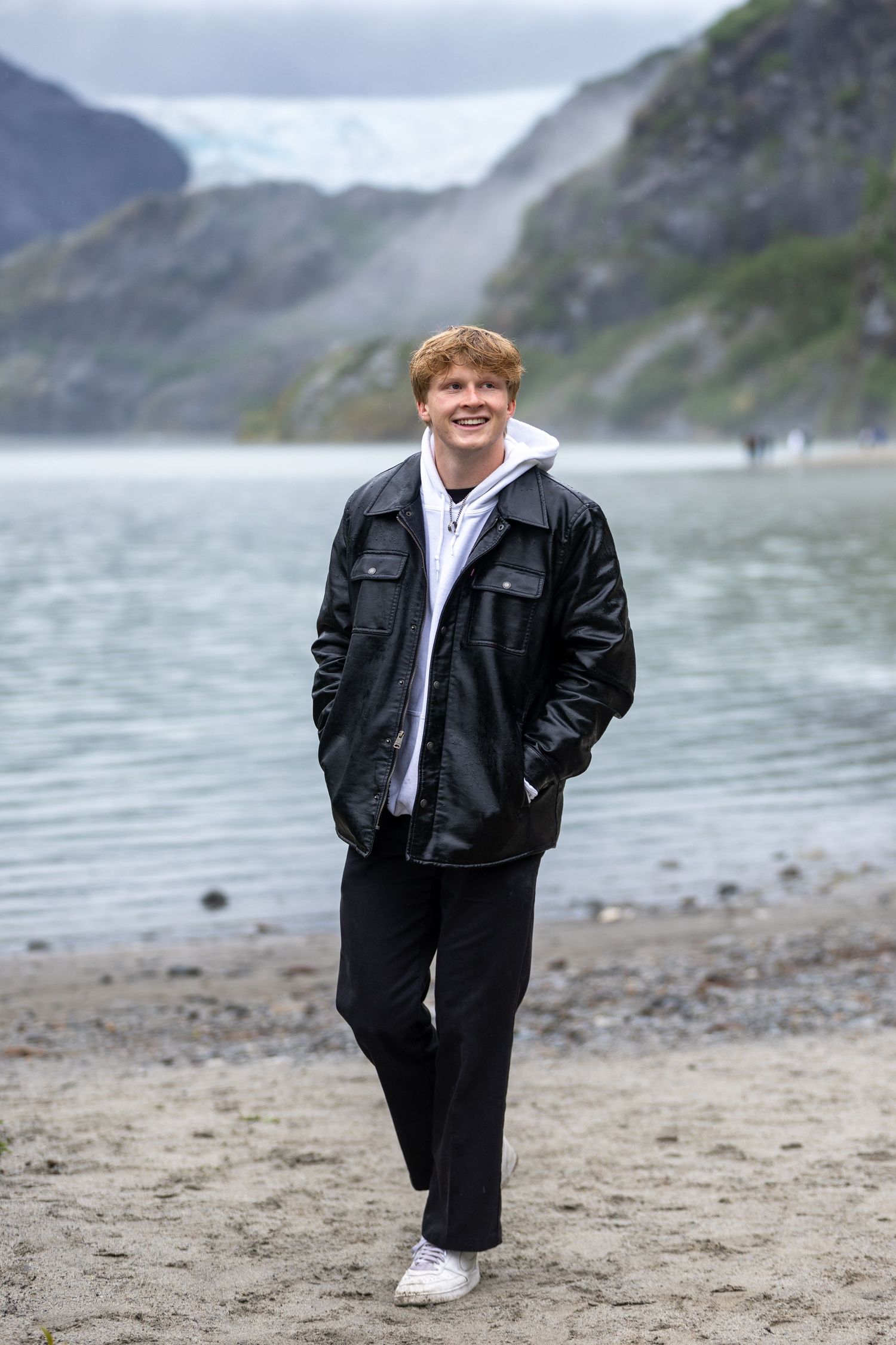 Person in black jacket poses on misty beach with rocky coastline in background.