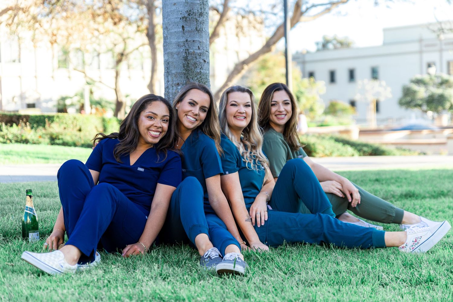 Healthcare graduates in blue scrubs pose together on grass during graduation photo session.