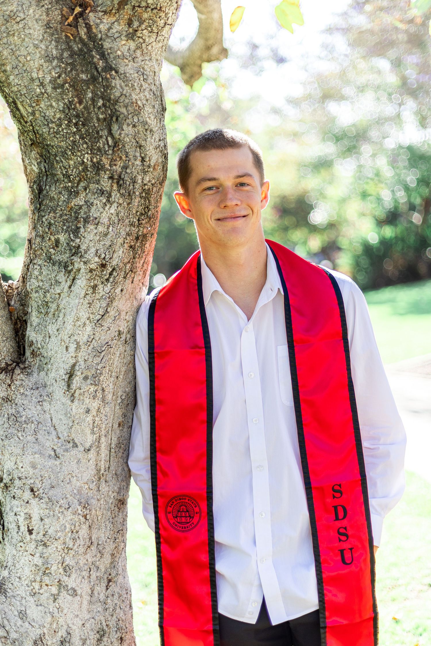 Graduation portraits taken outdoors featuring red stole against tree background.