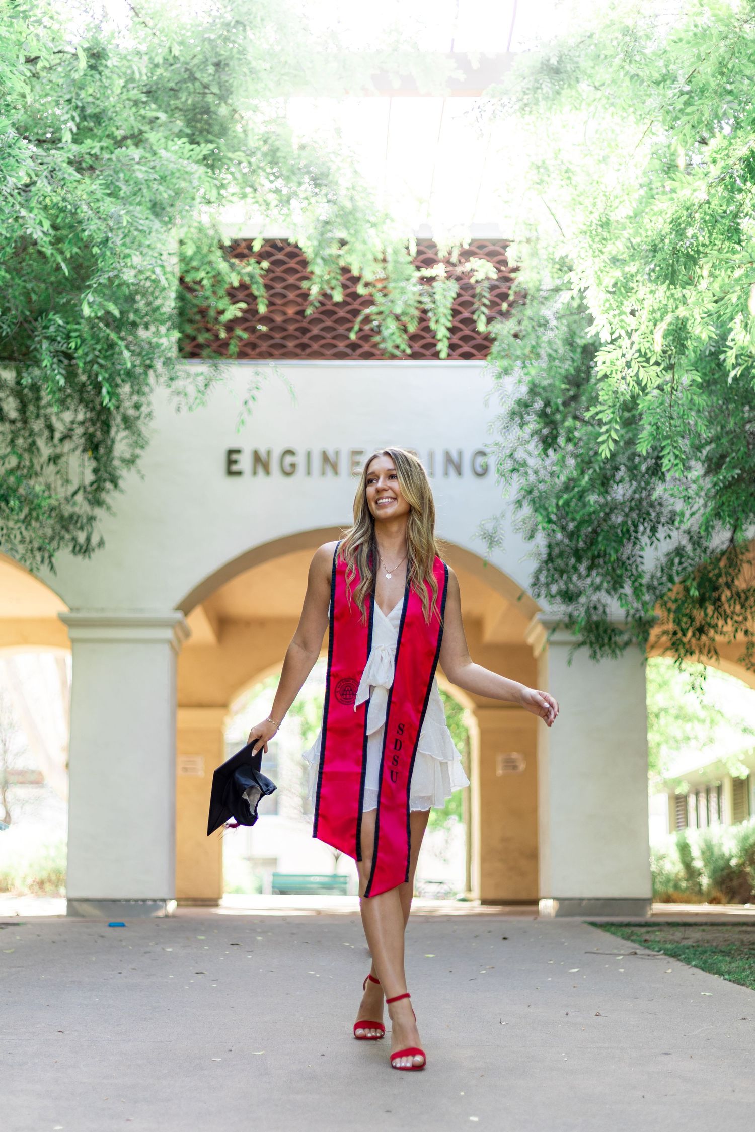 Graduate celebrates near Engineering building entrance in graduation regalia.