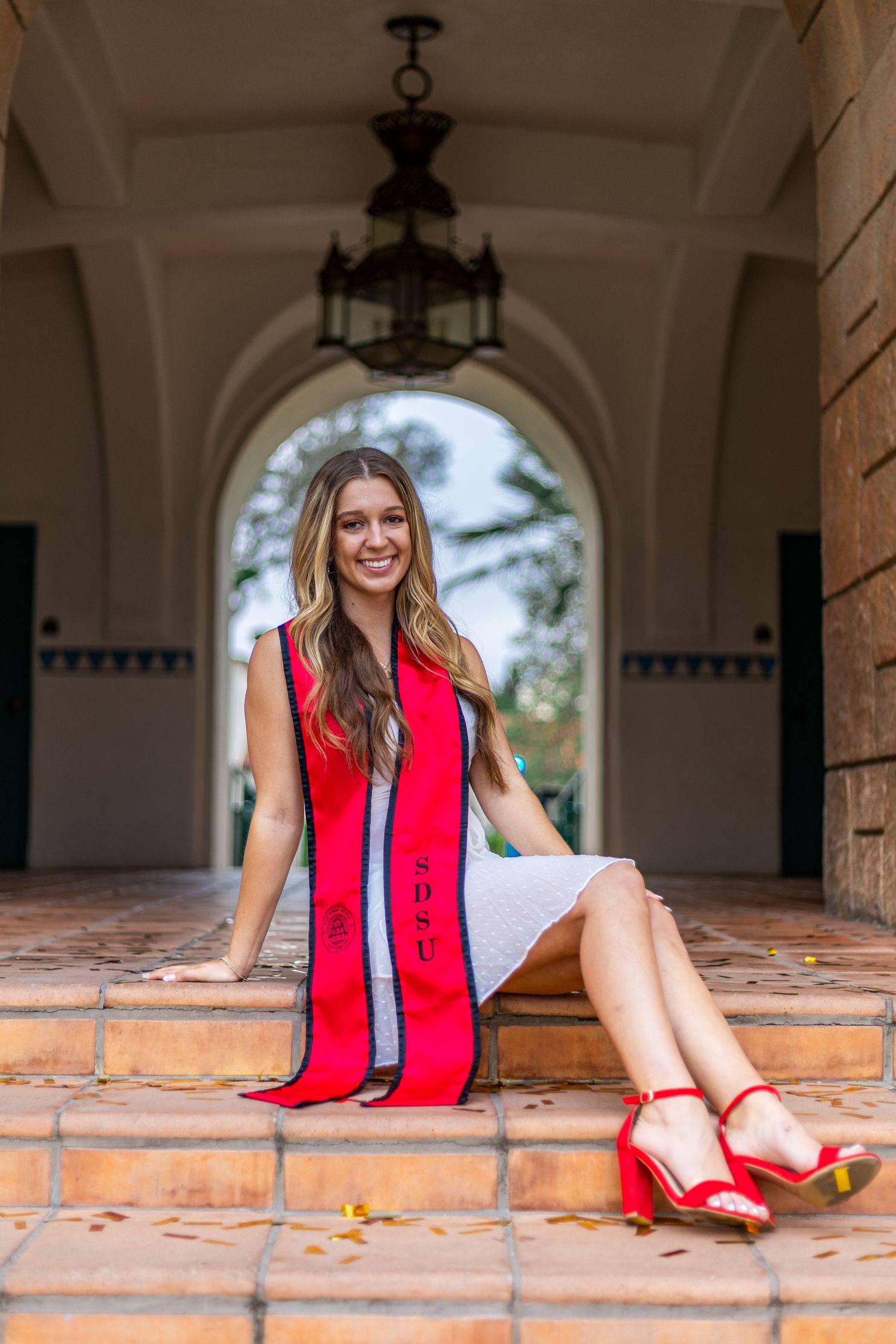 Graduate sitting in arched hallway wearing red stole and white dress.