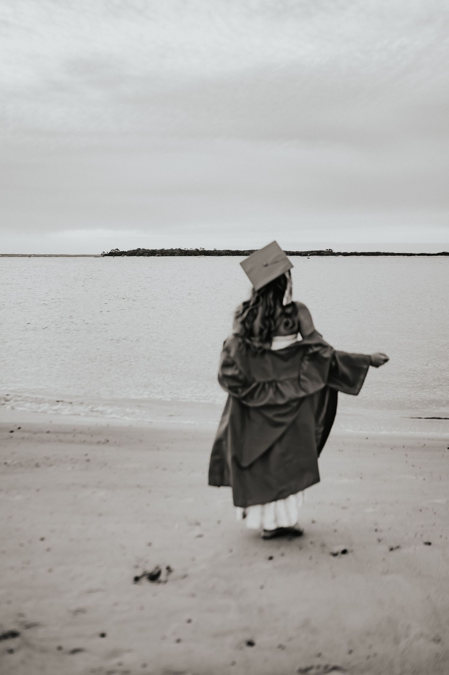 Senior girl beach photograph posing in her cap and gown on the beach in Fernandina Beach, FL