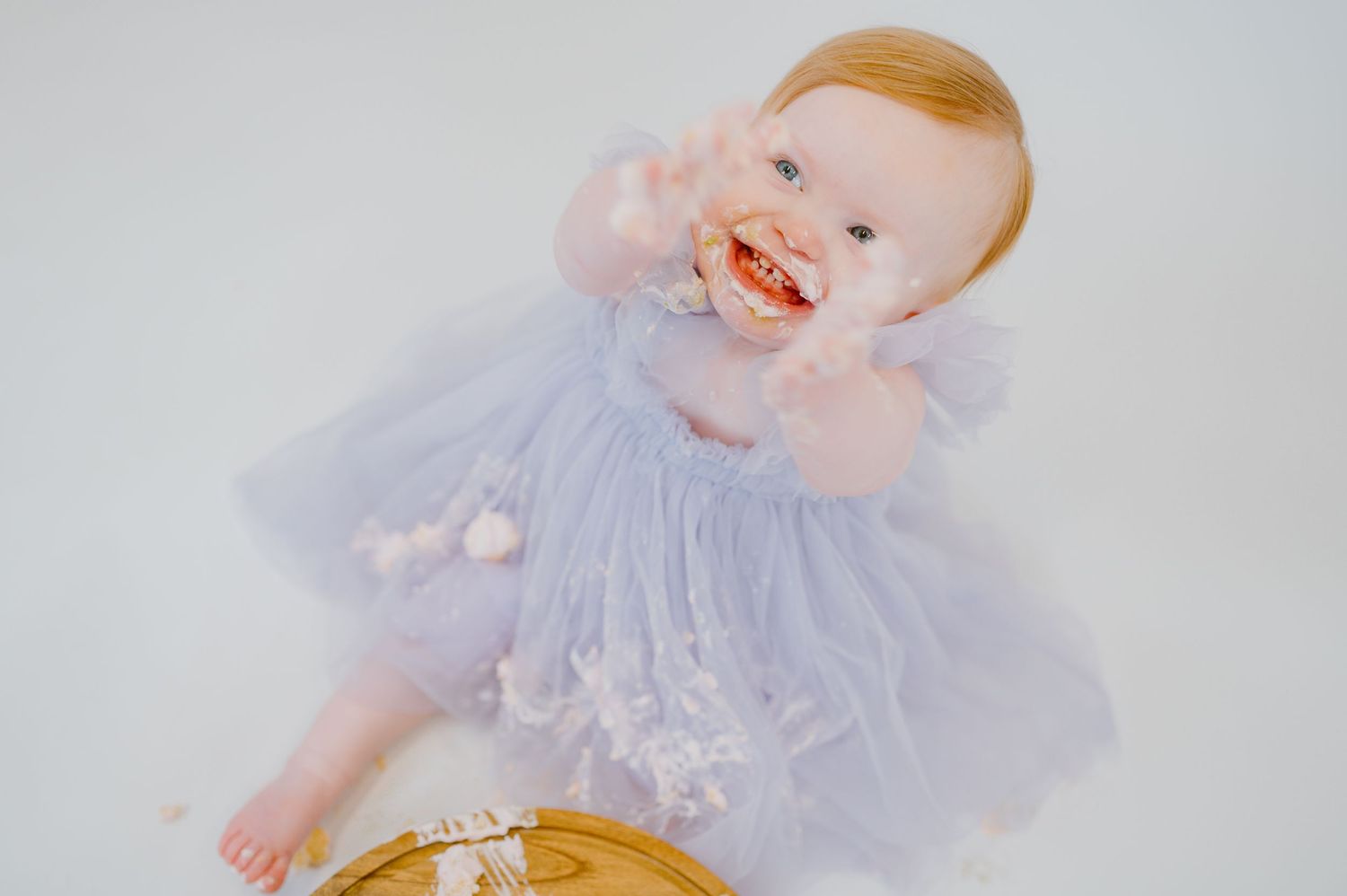 Smash cake photograph of a little girl for her first birthday photography session in a purple dress in studio in Fernandina Beach, FL