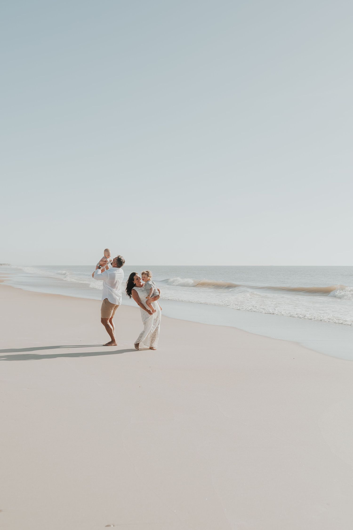 Family of four beach photo of dad tossing baby and mom dancing with child in a lifestyle dreamy background in Fernandina Beach Florida