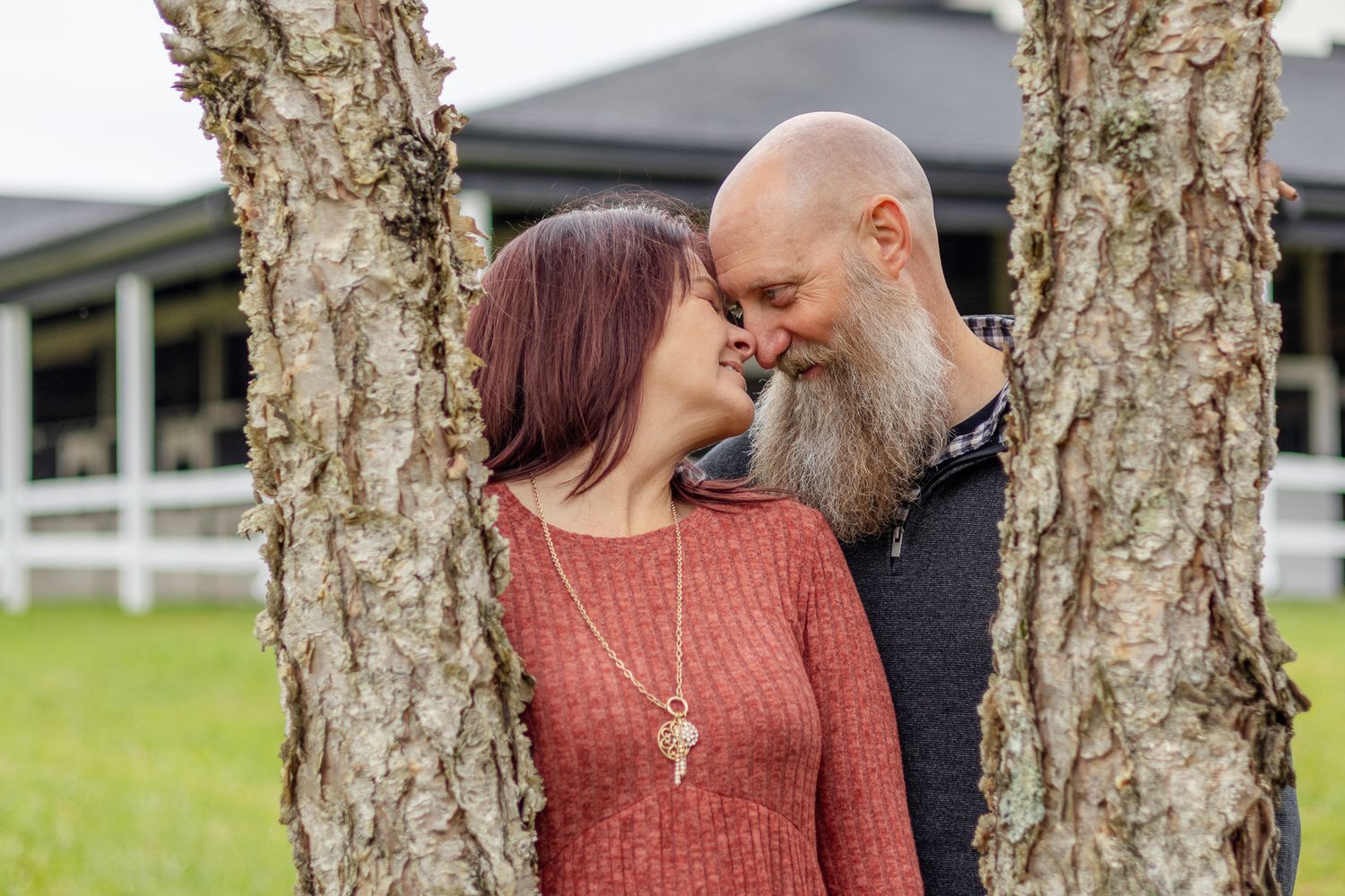 A couple poses between birch trees in a casual outdoor setting.