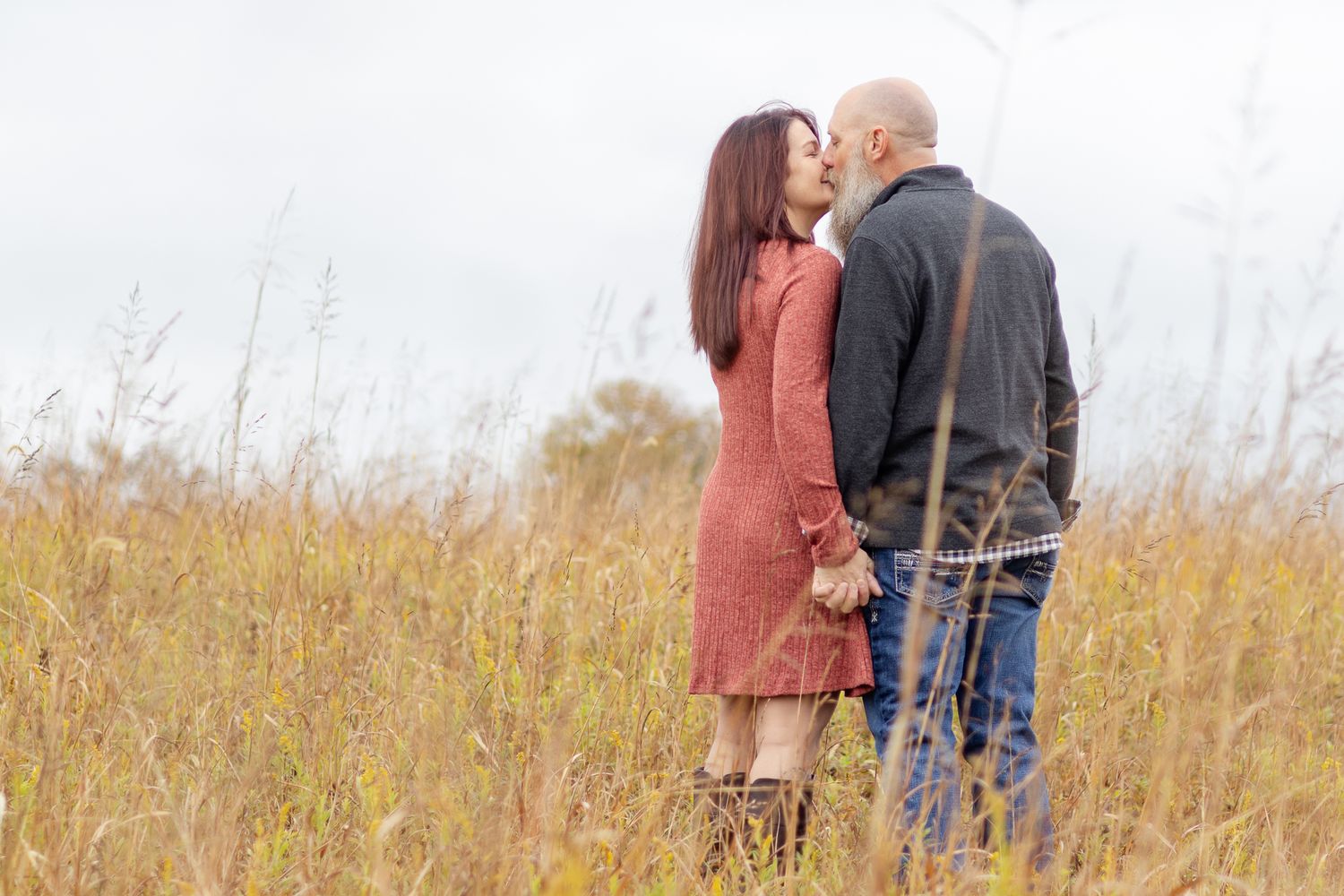 A couple embraces in a field of tall grass during golden hour.