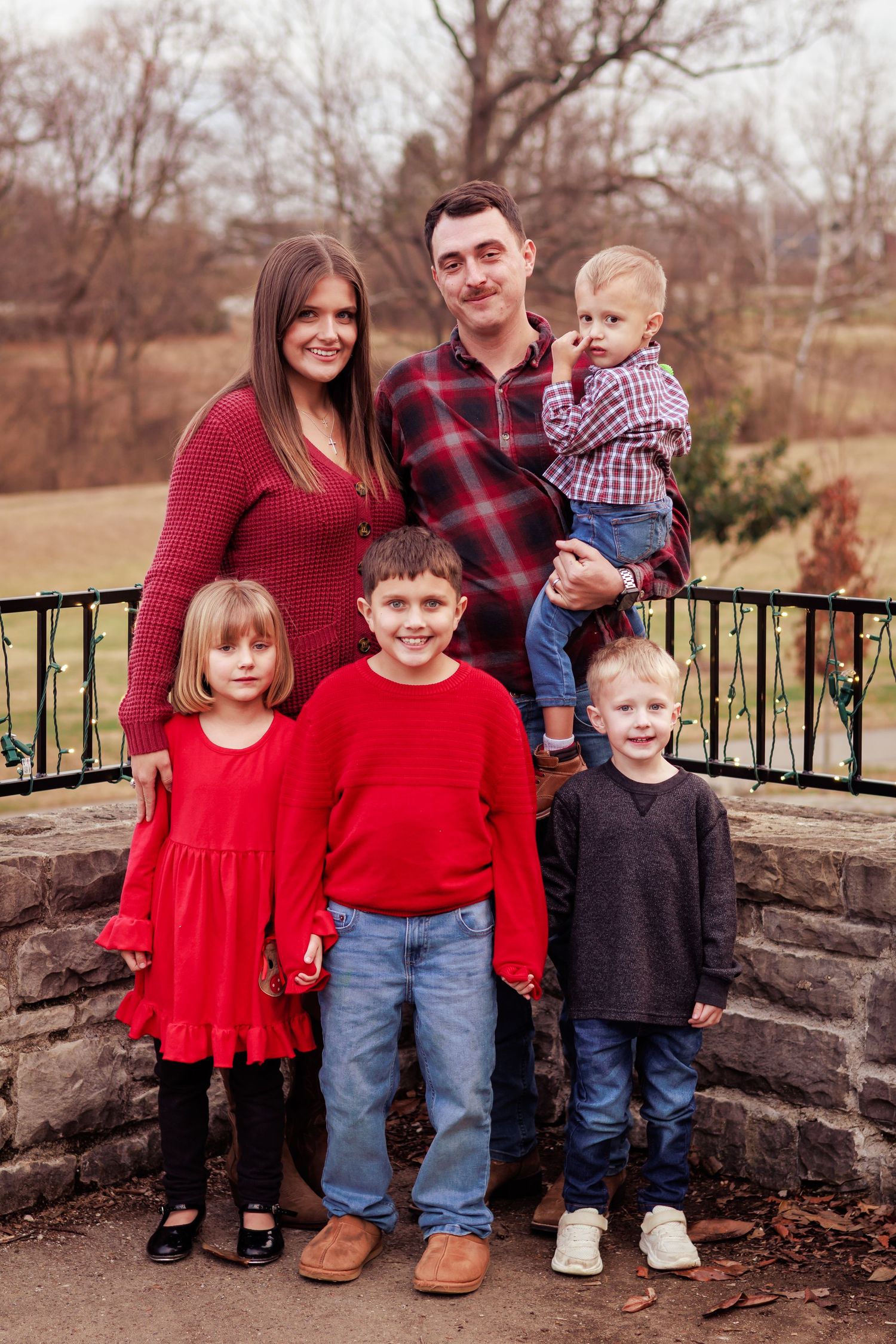 A family wearing red and plaid poses by a stone wall during autumn.