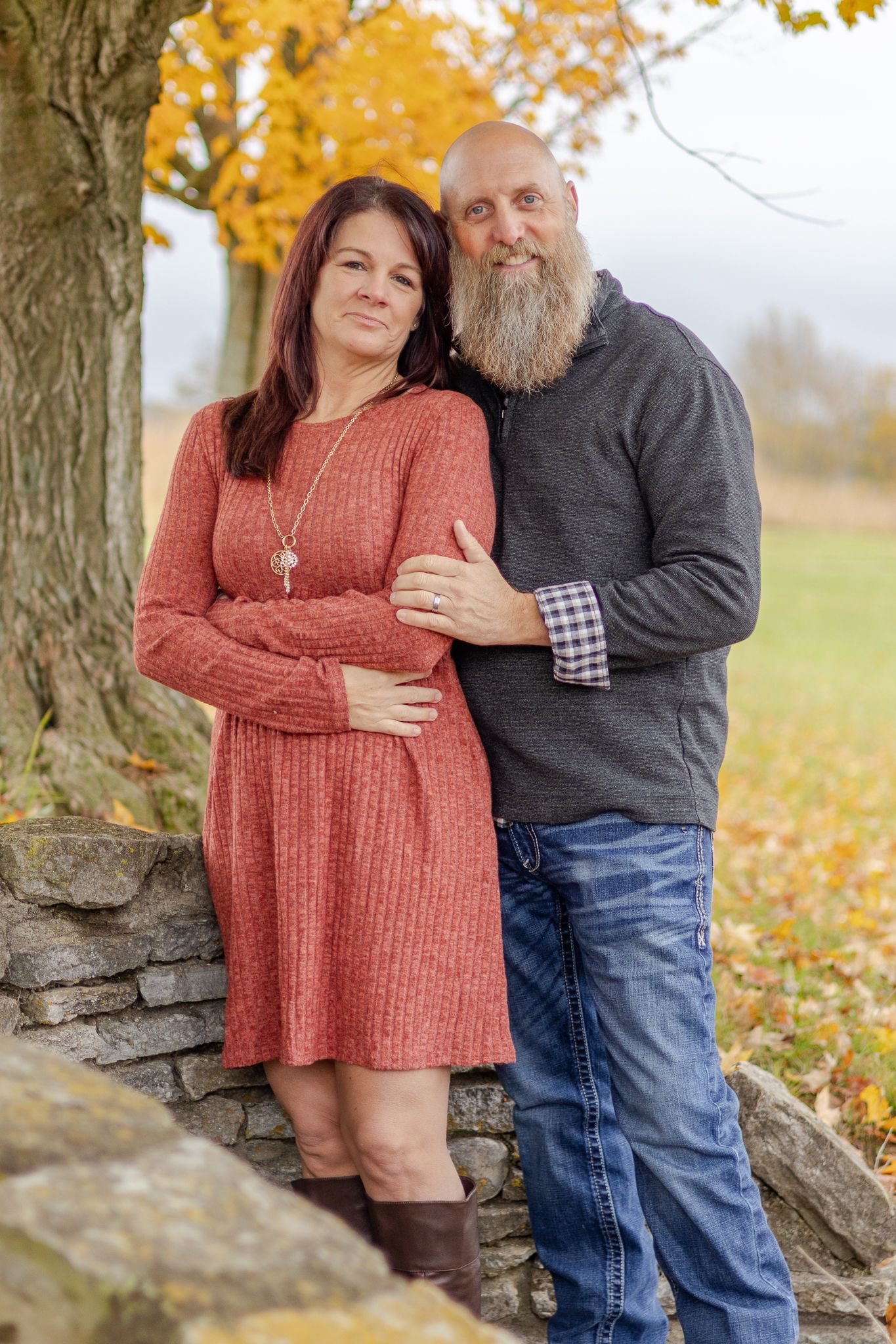 Couple shares intimate moment by stone wall with autumn leaves in background.