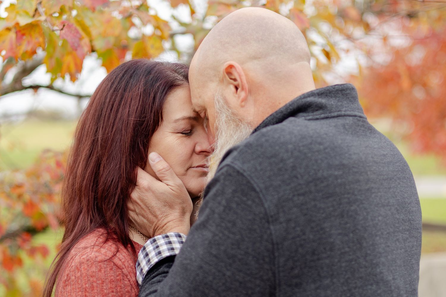 Romantic autumn couple embraces against colorful fall foliage in outdoor setting.