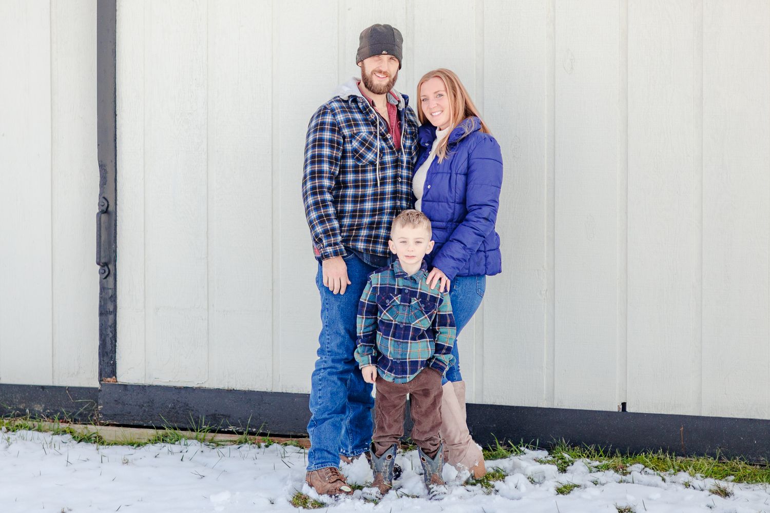 A winter family portrait against a white wall with snow on the ground.