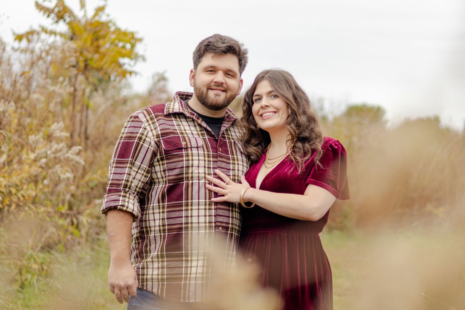 A couple embraces in an outdoor setting with golden autumn colors in the background.