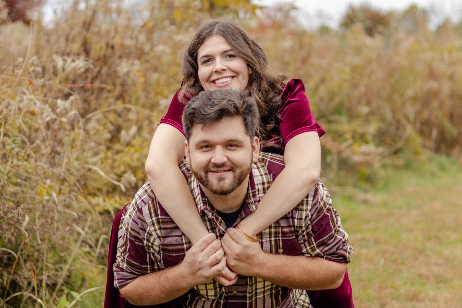 A couple shares a tender moment in a field with autumn foliage in the background.