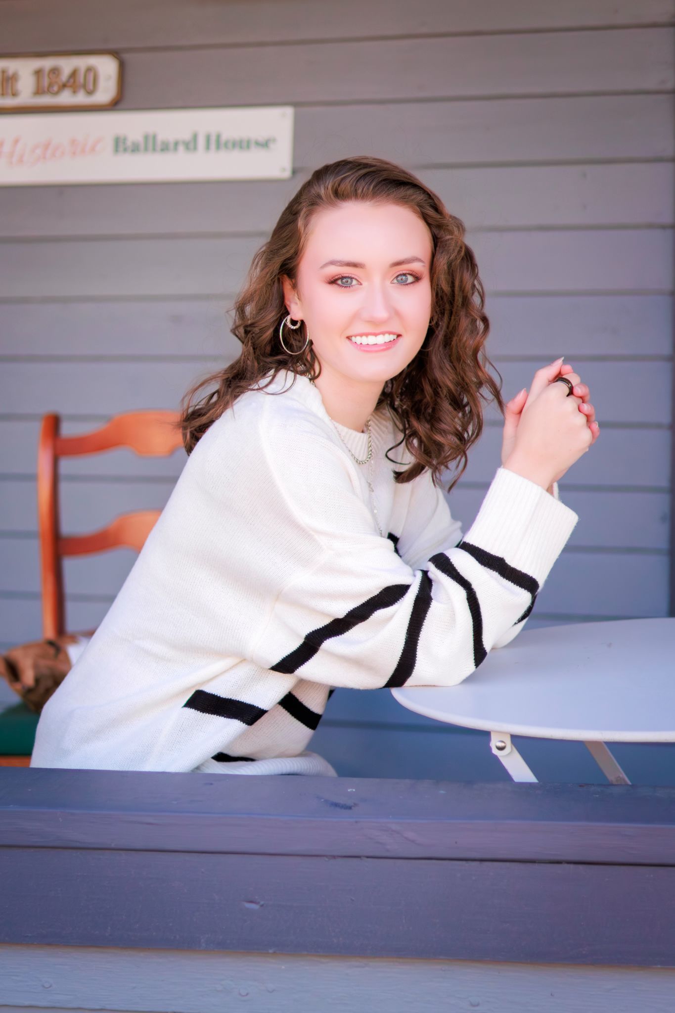 Woman in white blouse with black trim poses playfully on historic house porch.