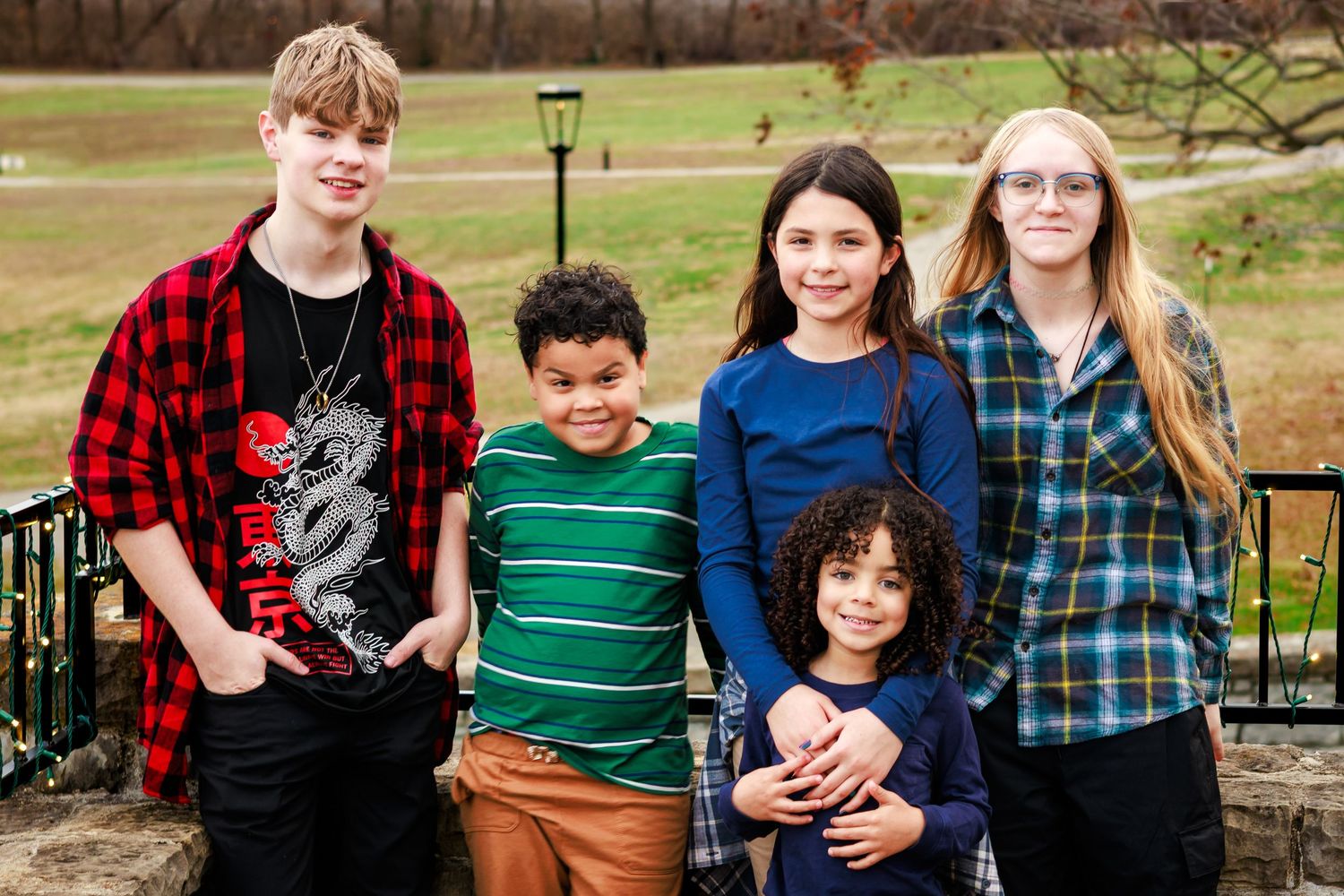Group of young people in casual attire standing together outdoors near a lamp post.