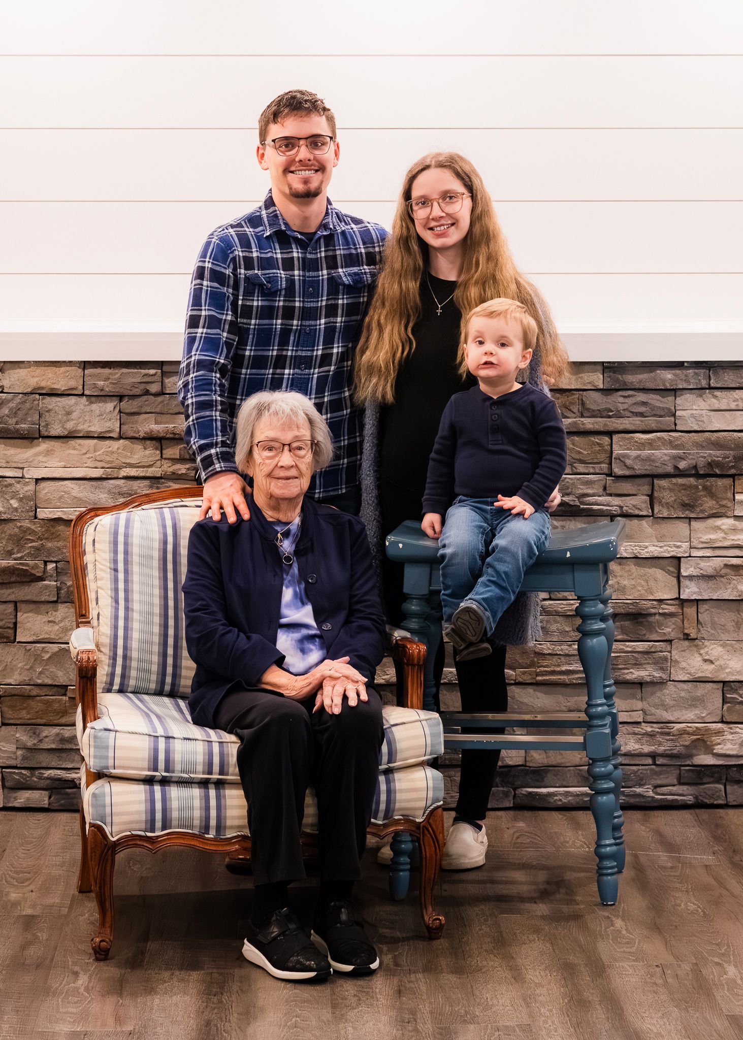 Multi-generational family portrait with stone wall background and blue accent chair.