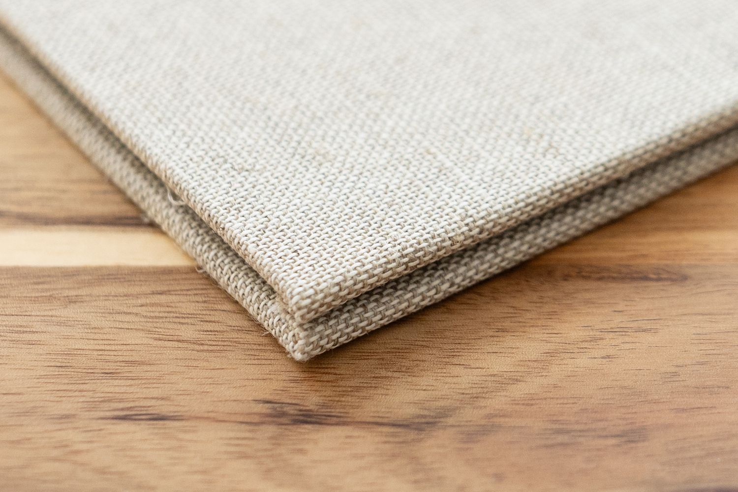 Gros plan sur une toile en lin naturel pliée et tendue sur un châssis en bois, reposant sur une surface en bois rustique.