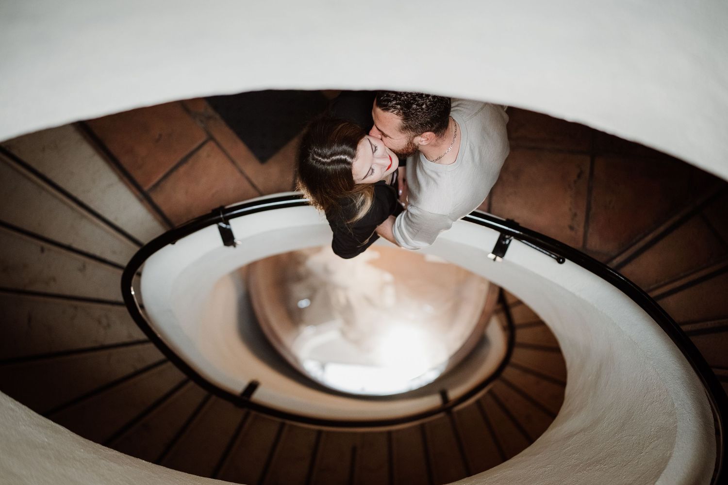 Vue aérienne d'un couple partageant un moment romantique sur un élégant escalier en colimaçon aux murs blancs.