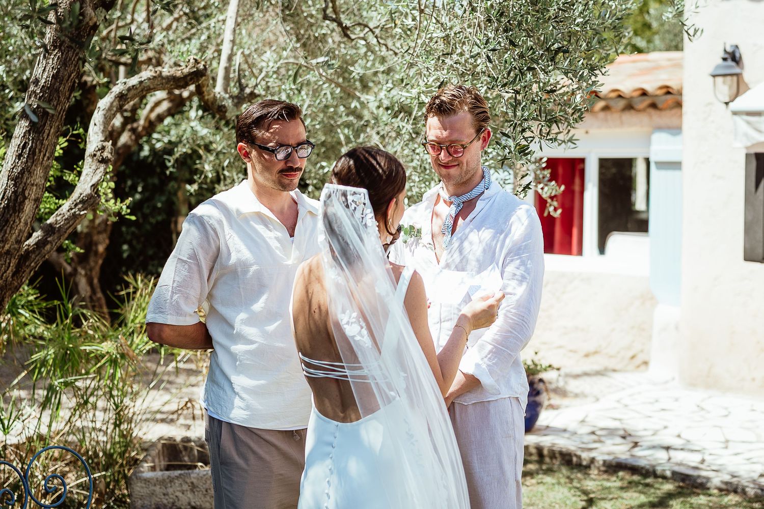 Une mariée en robe blanche et voile échange ses vœux avec le marié en plein air, près d'oliviers, lors d'un mariage méditerranéen ensoleillé