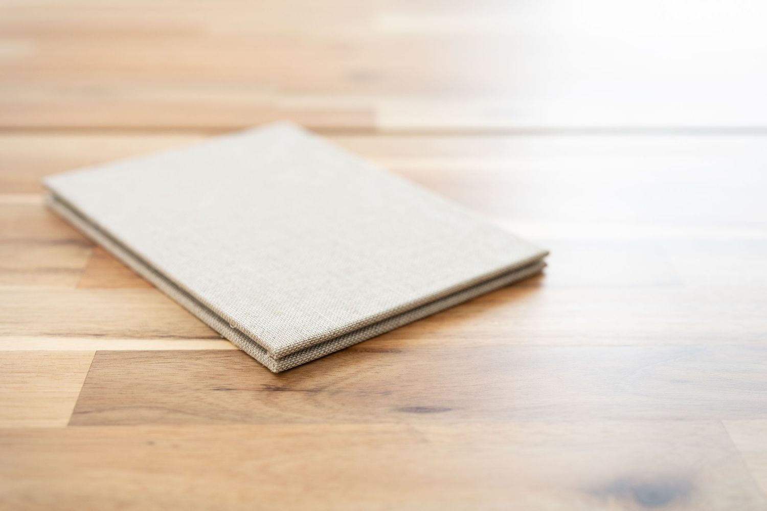 Un carnet fermé, recouvert de lin beige, posé sur une table en bois clair.
