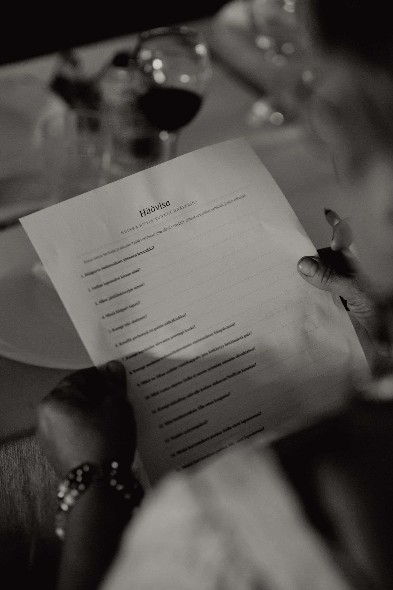 Person holding a printed questionnaire at a dinner table with wine glasses in black and white photo.