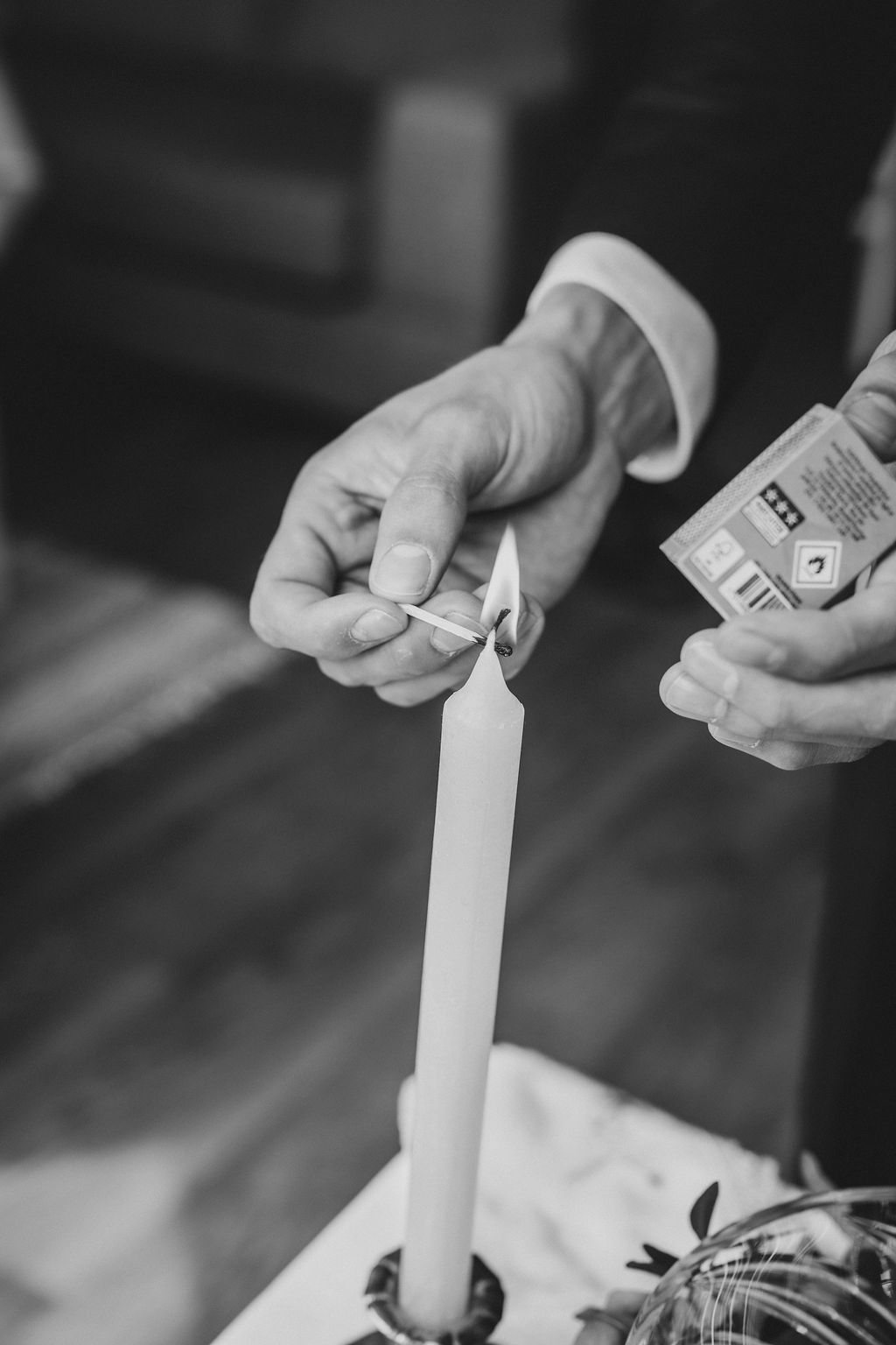 Black and white photo of hands lighting a tall white candle with a match during a ceremony.