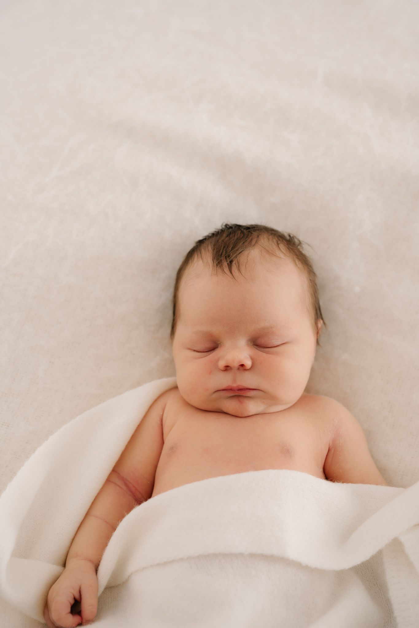 Peaceful newborn baby sleeping on a soft white blanket, with dark hair and delicate features.