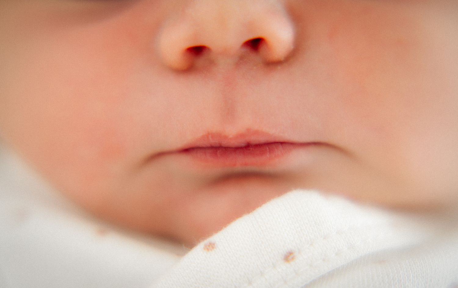 Close-up of a newborn baby's nose and lips, showcasing delicate infant features against a soft white background.