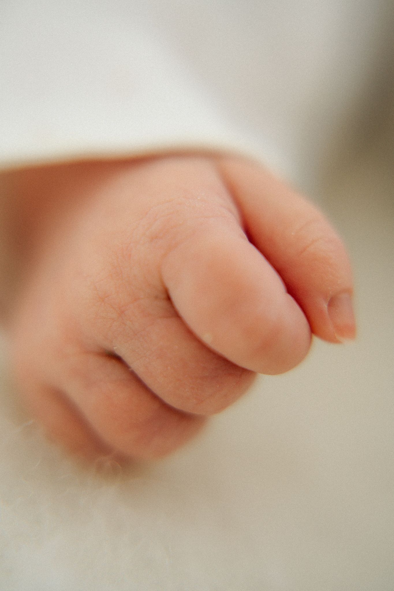 Close-up of a newborn baby's tiny clenched fist resting on a soft white blanket.