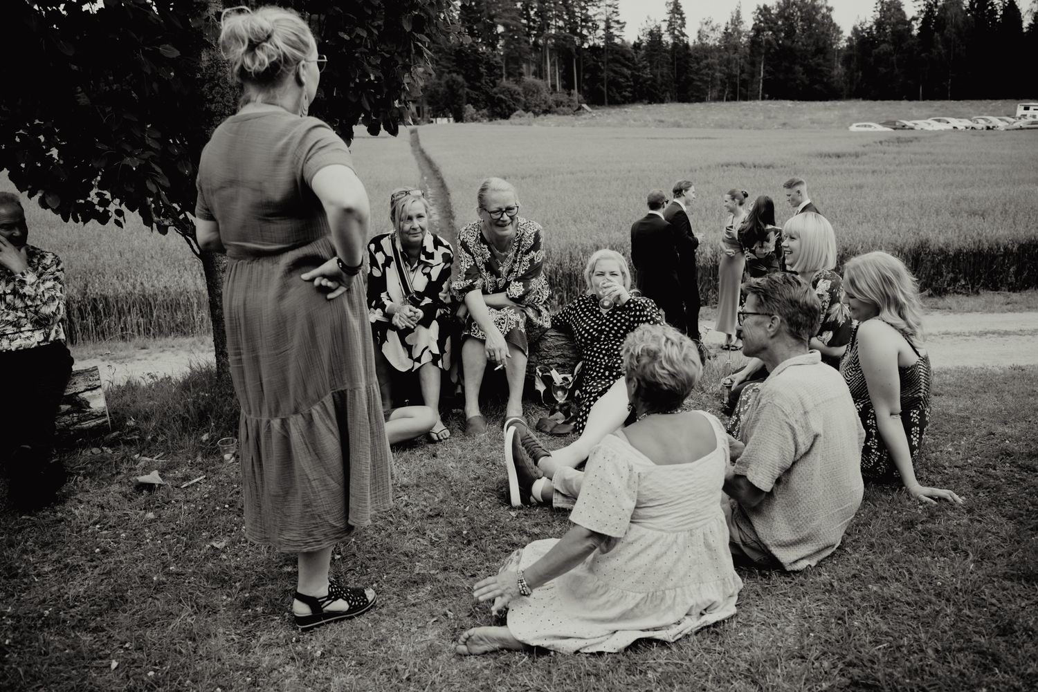 Black and white photo of women and children gathered outdoors on grass, socializing at a rural summer gathering.