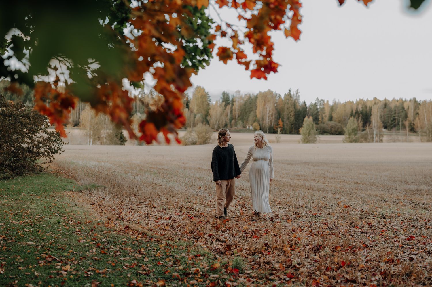 Autumn family photoshoot with fallen red leaves in a park setting.