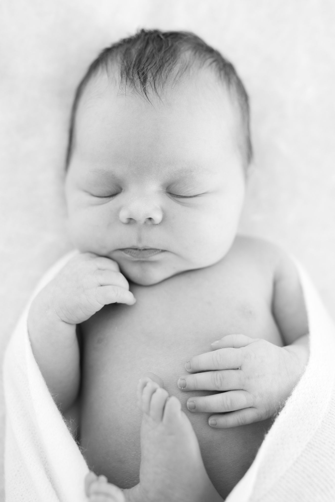 Black and white photo of a peaceful sleeping newborn baby wrapped in a white blanket.