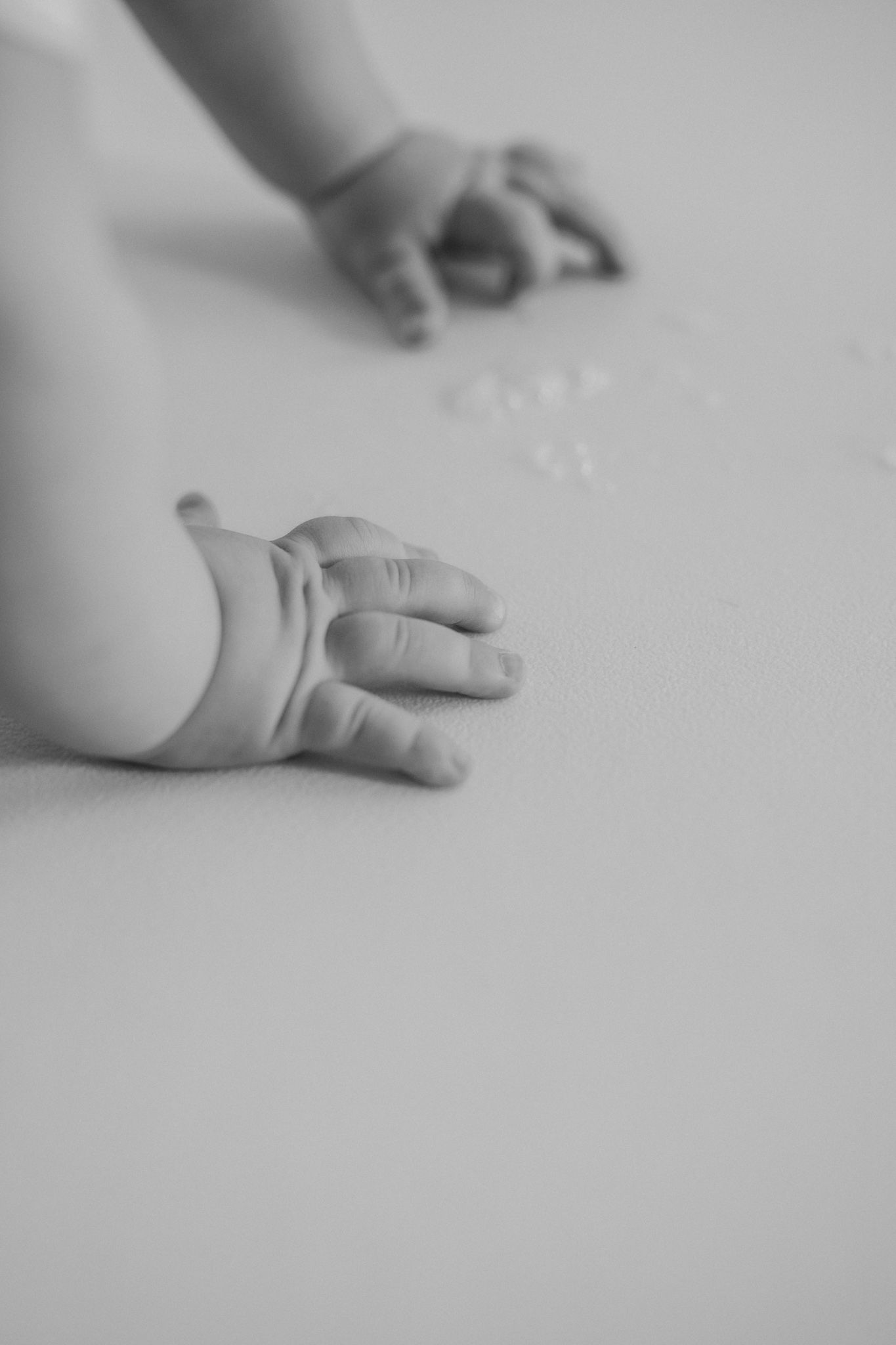 Black and white close-up photo of a baby's tiny hands resting on a soft white surface.