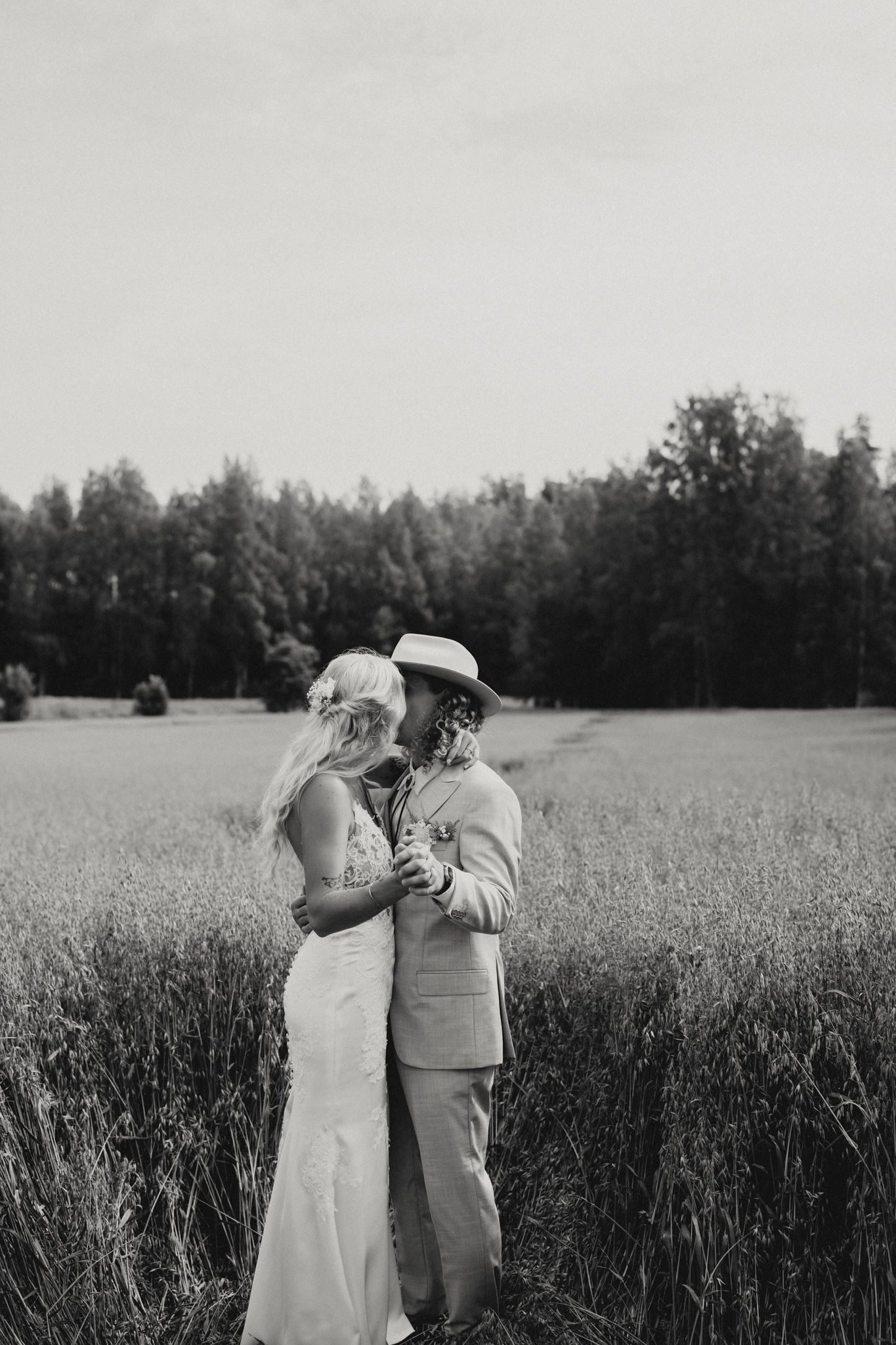 Black and white photo of a bride and groom embracing in a field with trees in the background.