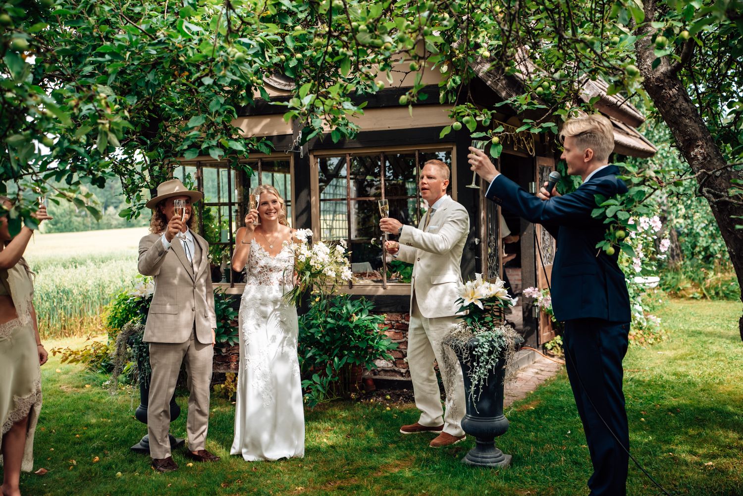 Outdoor wedding celebration with bride and groom toasting champagne surrounded by guests near a rustic wooden building.
