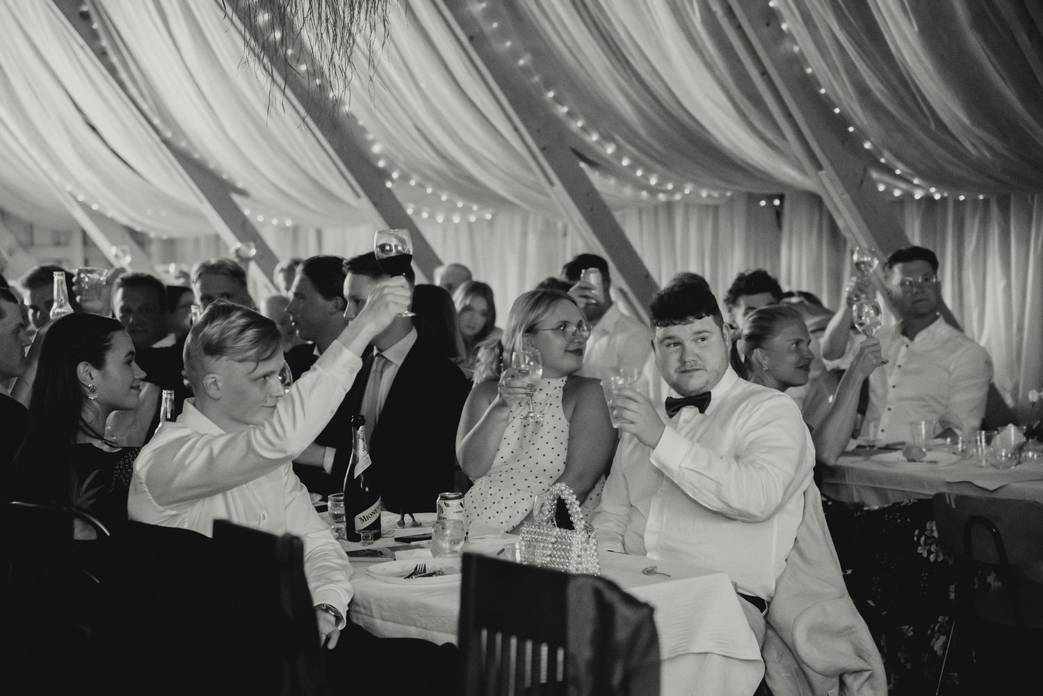 Black and white wedding reception photo of guests celebrating under draped fabric ceiling with twinkling lights.