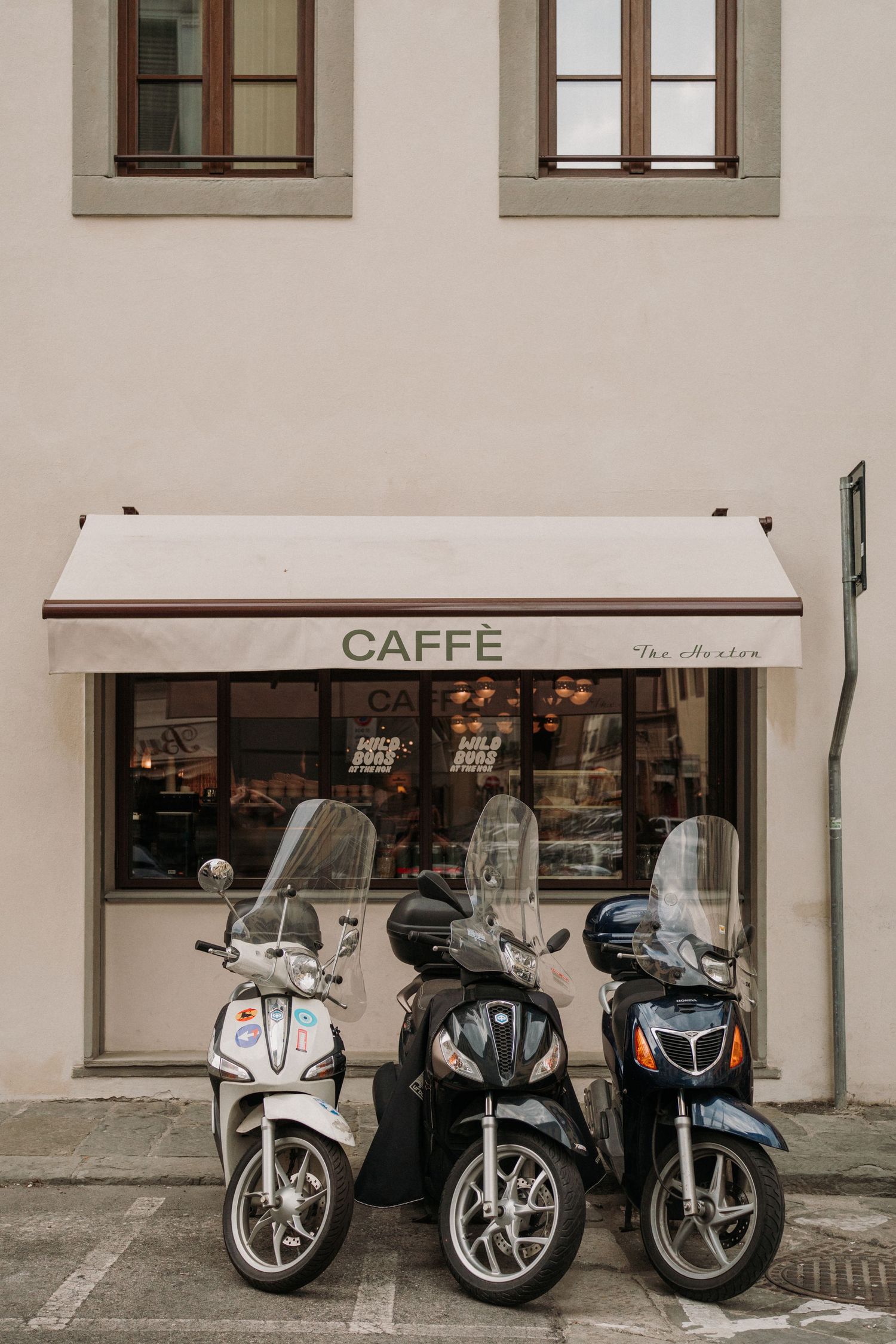 Three scooters parked in front of a European caffe with a striped awning.