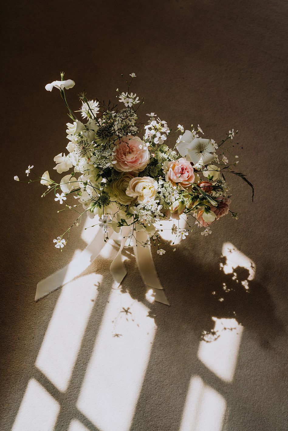 Romantic bridal bouquet with pink roses and white wildflowers casting shadows in warm natural light.