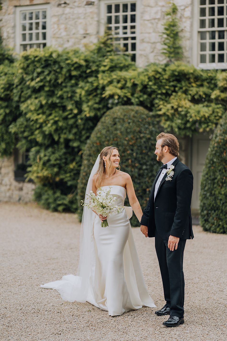 Bride and groom holding hands in front of an ivy-covered stone building on their wedding day.