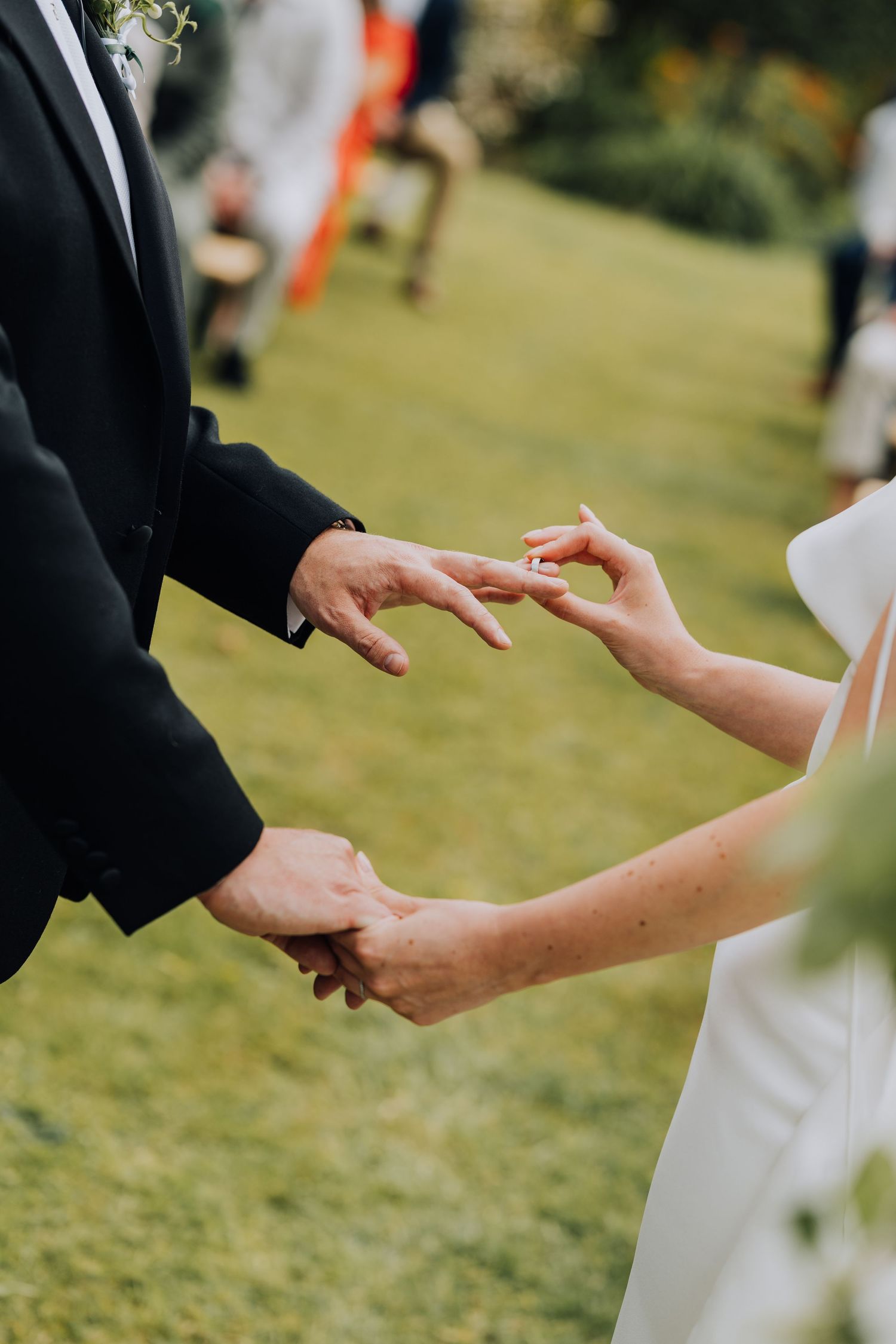 Close-up of bride placing wedding ring on grooms finger during outdoor garden ceremony.
