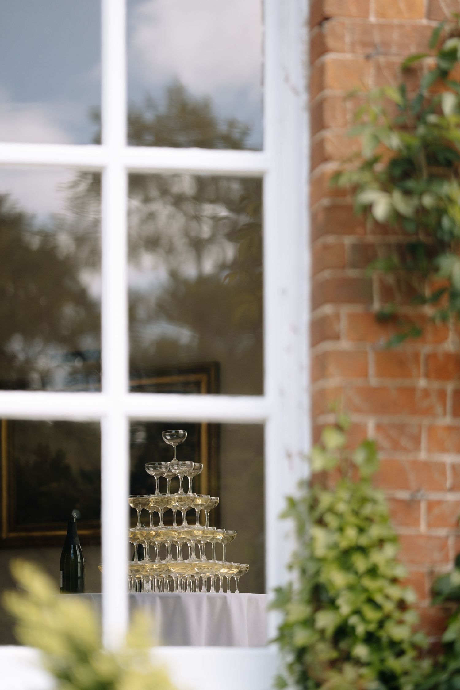 Elegant champagne tower displayed in front of a white-framed window at a wedding venue with brick walls.