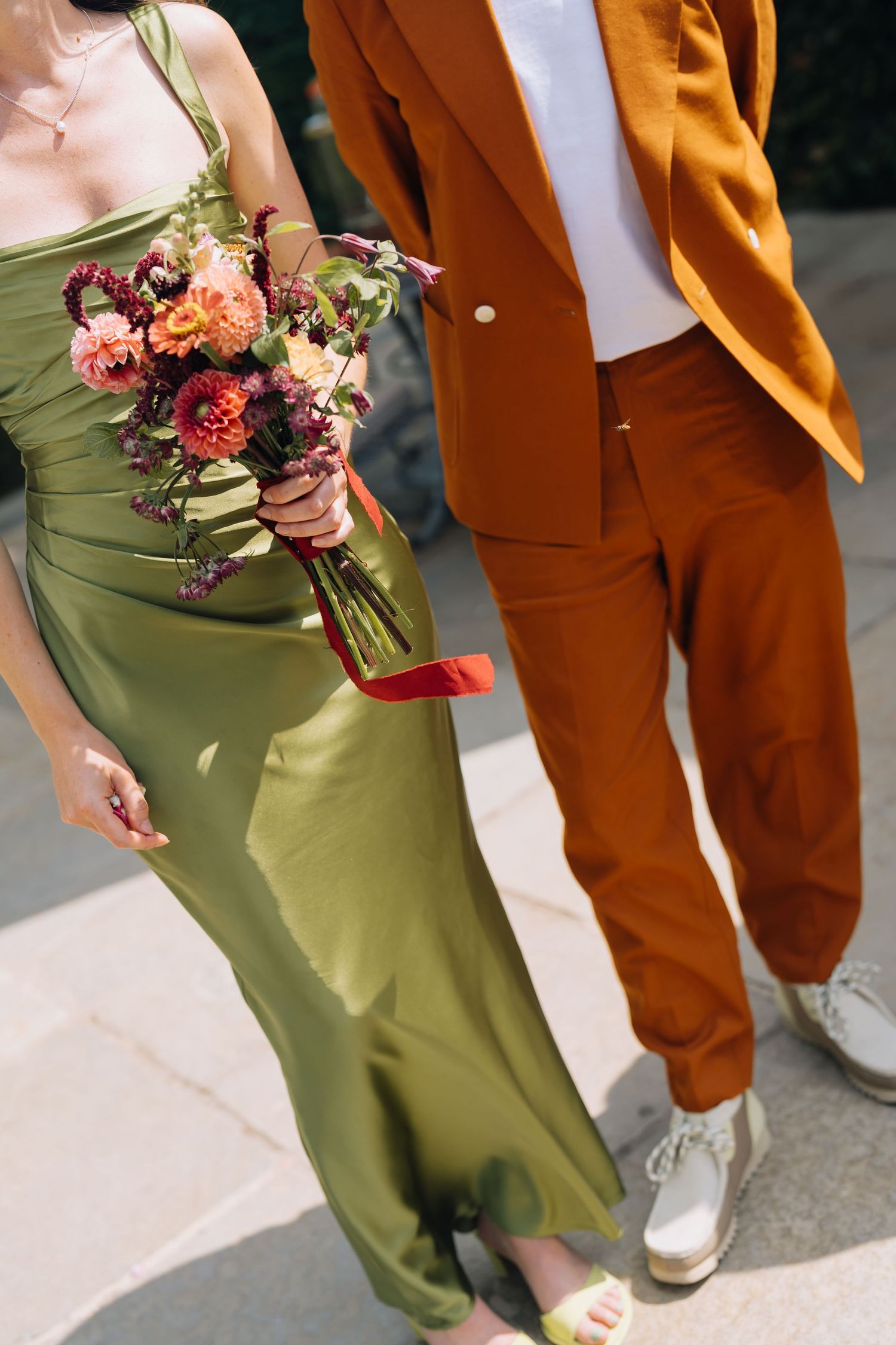 Couple walking together, woman in green satin dress holding colorful bouquet, man in burnt orange suit.