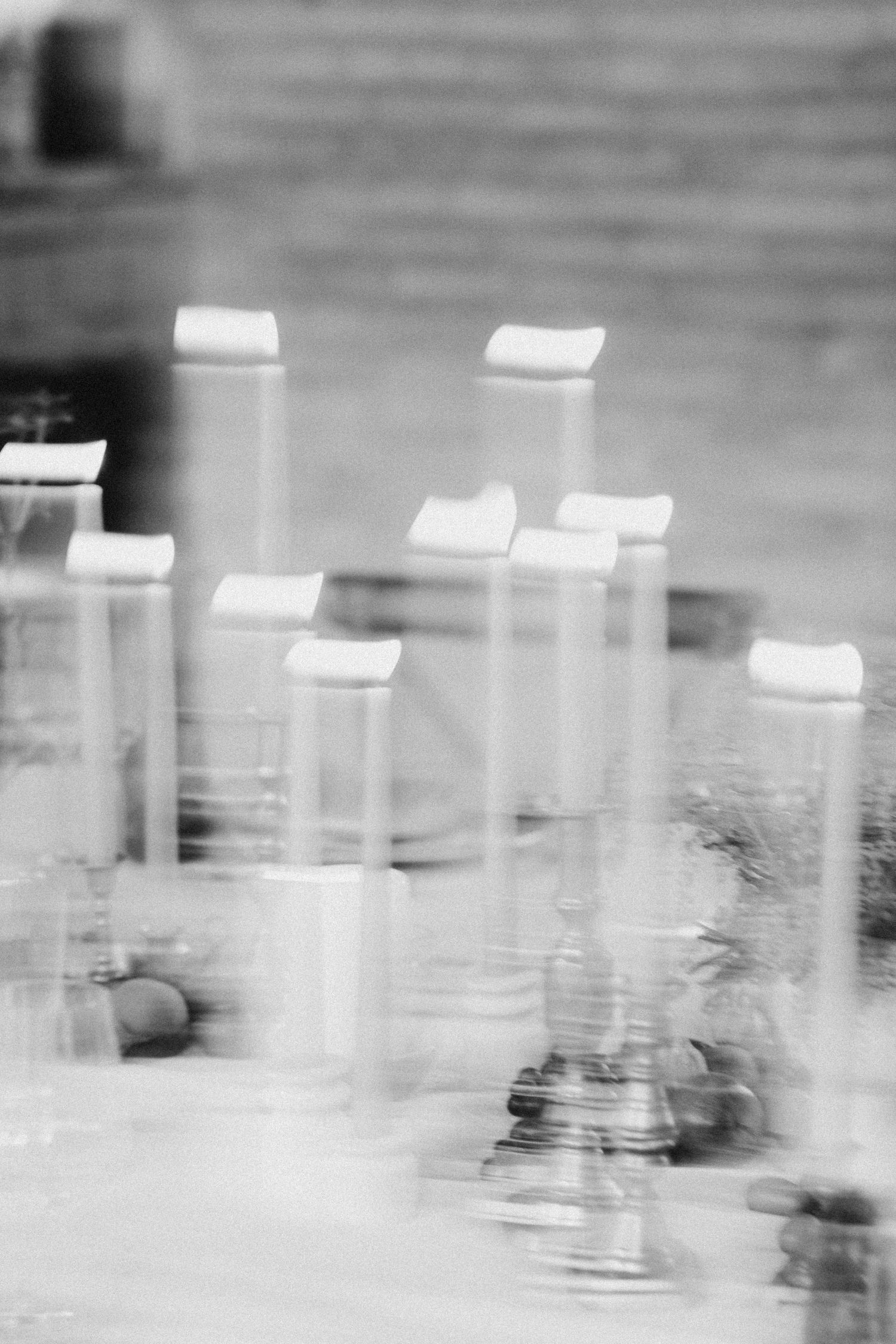 Black and white blurred artistic shot of tall glass candle holders on a wedding table.